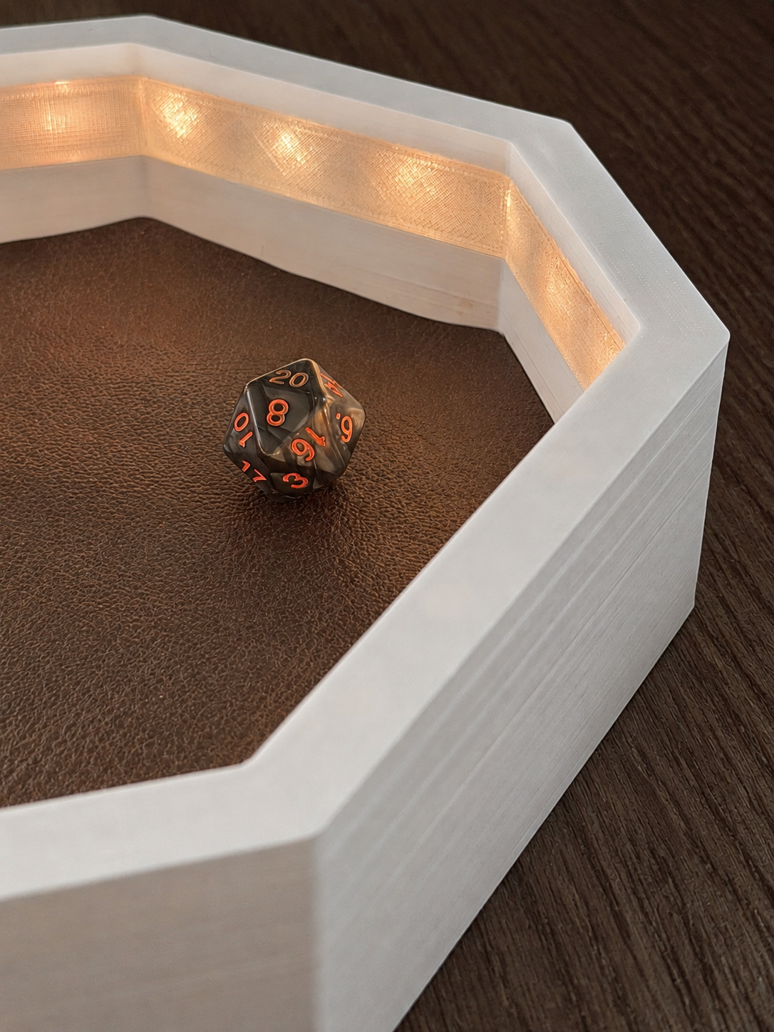 Close-up of warm LEDs diffusing through the inner wall of an OmniRoll Origin prototype beside a physical d20